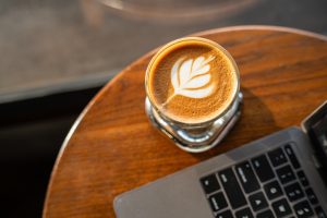 Close-up of Hot coffee latte with latte art milk foam in cup mug and laptop computer on wood desk office desk in coffee shop at the cafe,during business work concept